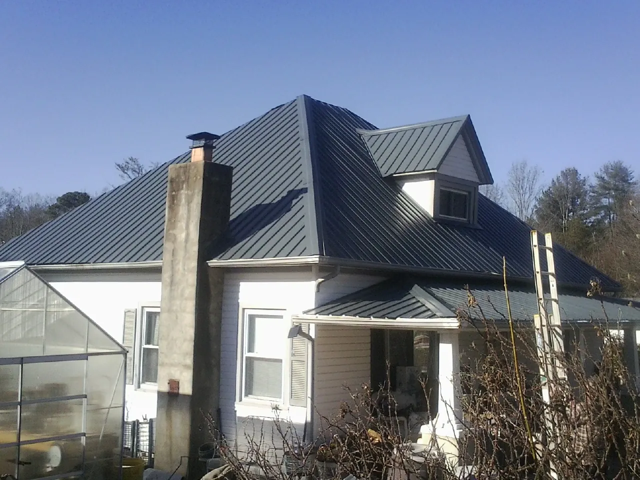 Dark blue standing seam metal roof on a white farmhouse with dormer — Slate & Tile Roof Repair by Roofing Brothers in Middle River