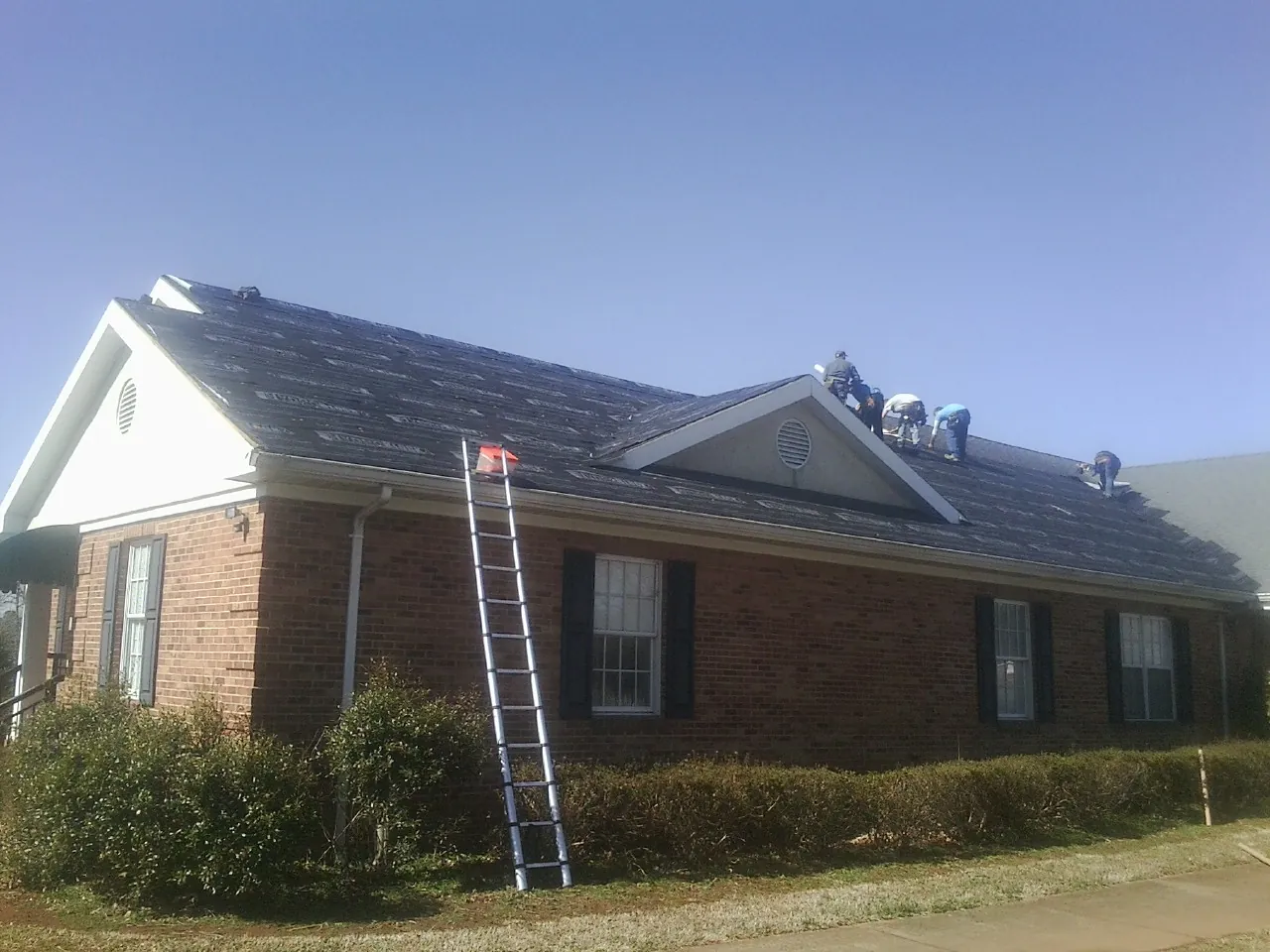Crew tearing shingles off a brick ranch roof with a ladder set — Metal Roof Repair work by our crew in Middle River
