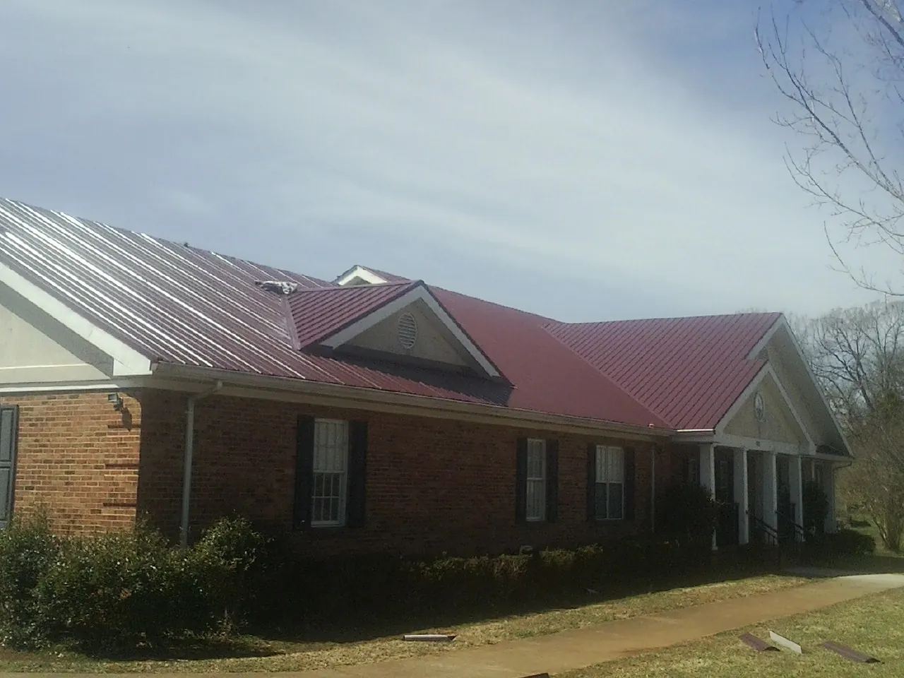 Red metal roof with gabled entries on a long brick building, from a Hail Damage Roof Repair job in Middle River