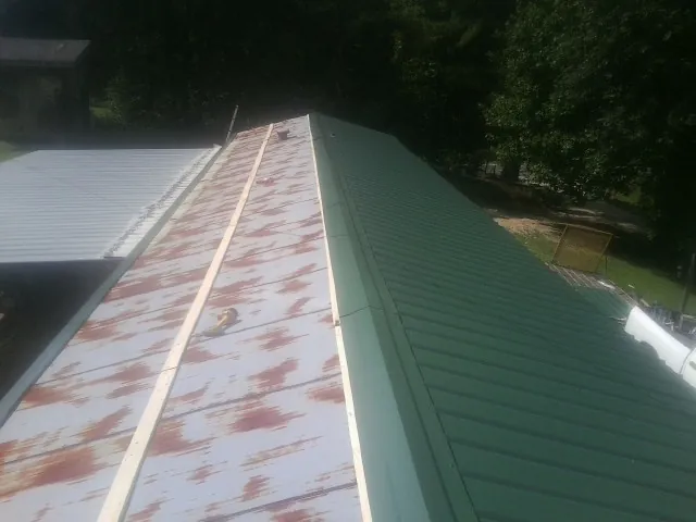 Old rusted panels beside newly installed green metal roofing — Wind Damage Roof Repair by Roofing Brothers in Middle River