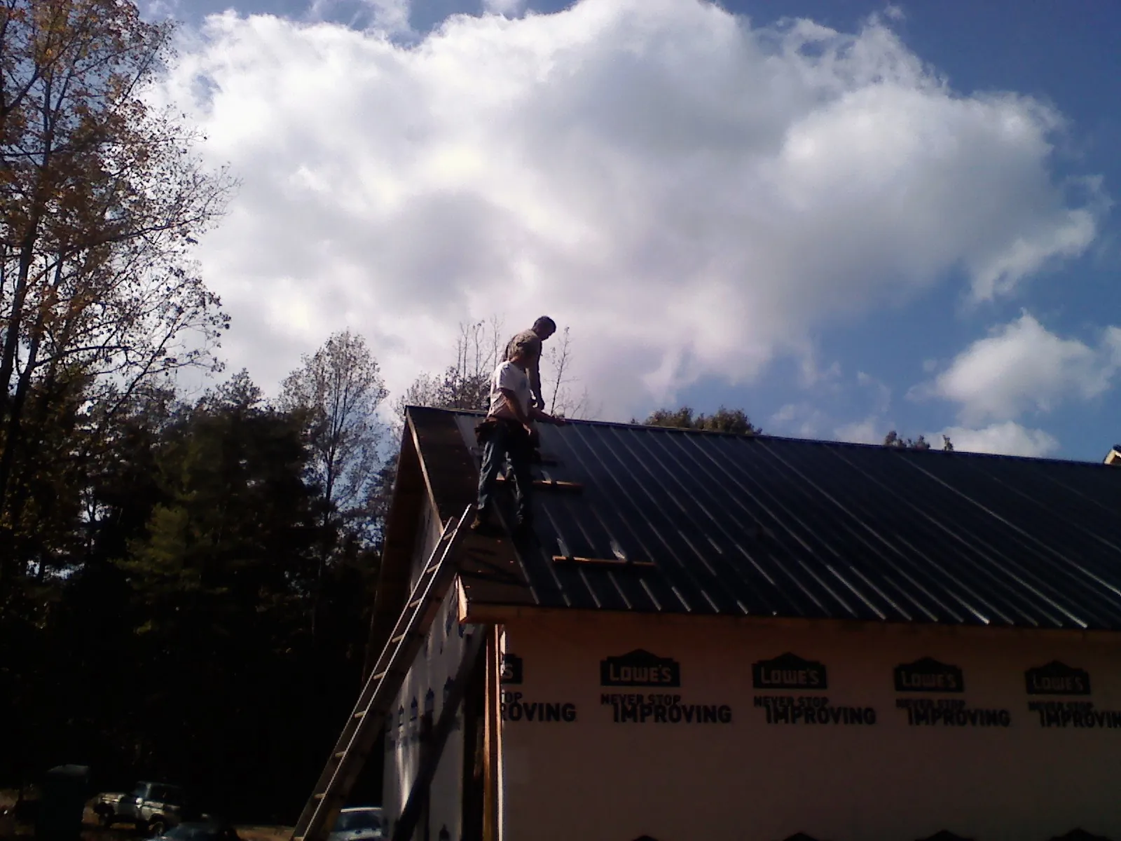 Roofer fastening dark metal panels high against a cloudy sky, from a Roof Inspection job in Middle River